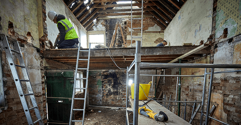 Wide shot of a derelict building with construction men working on it.