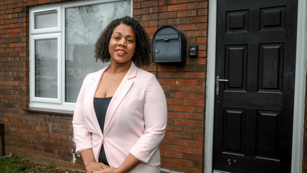 Caribbean woman in pink suit stood outside of a property