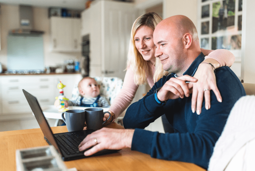 Happy couple looking at a laptop with their baby in a highchair