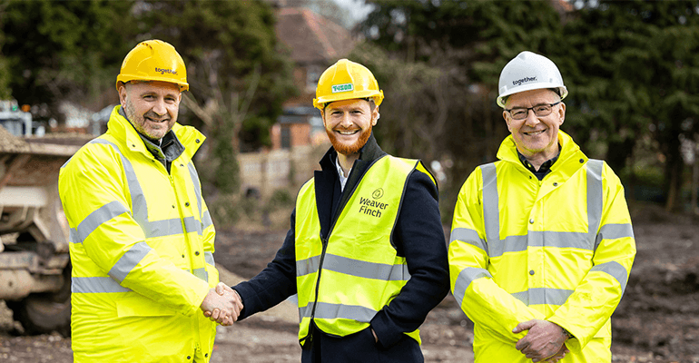 Three men in high visibility vests and hard hats smiling and shaking hands.