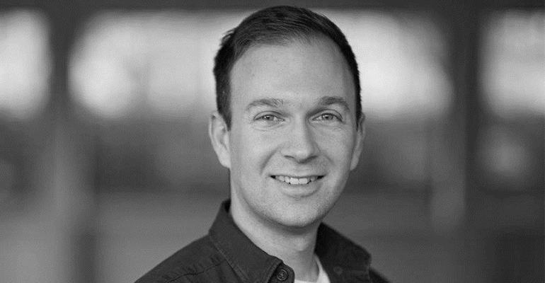 A close up black and white photo of a man with short hair smiling.