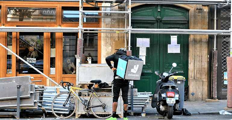 A Deliveroo cyclist putting on his bag on a street.