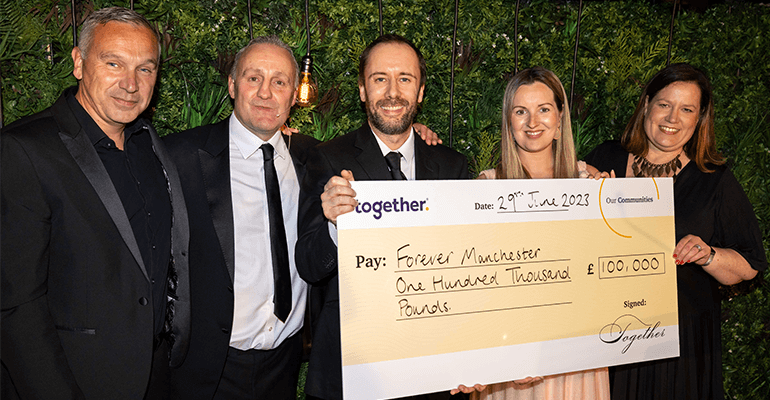 A group of colleagues holding a cheque for one hundred thousand pounds.