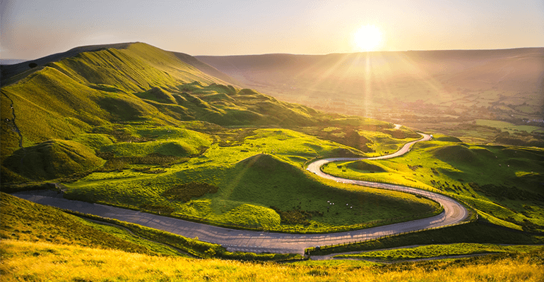 A long shot of a windy country-side road with the sun setting in the hills.