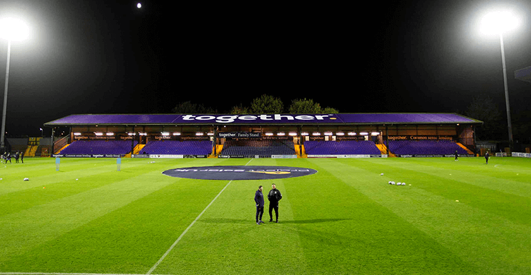 A long shot of Stockport county football club at night with two footballers stood in the center of the field.