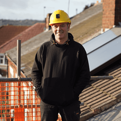 A man wearing all black with a yellow hardhat on on top of a roof.