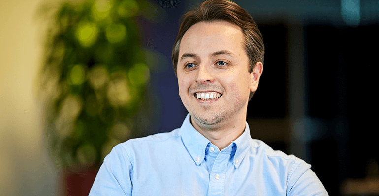 A man with short brown hair smiling wearing a light blue shirt.