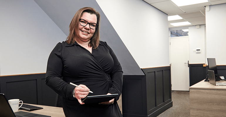 A woman sat on a desk with an ipad smiling.