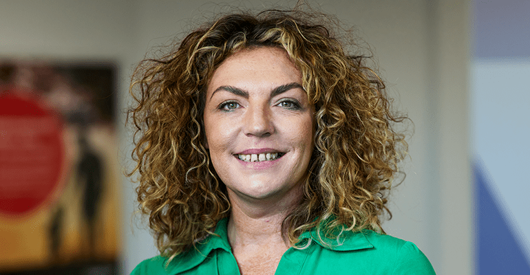 A woman with blonde and brown hair smiling wearing a green blouse.