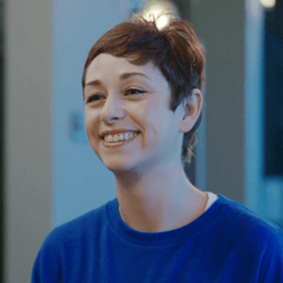 A woman with short brown hair smiling wearing a blue jumper.