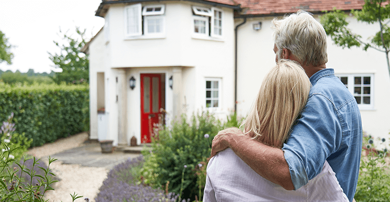 An older couple cuddling whilst looking at a new house.