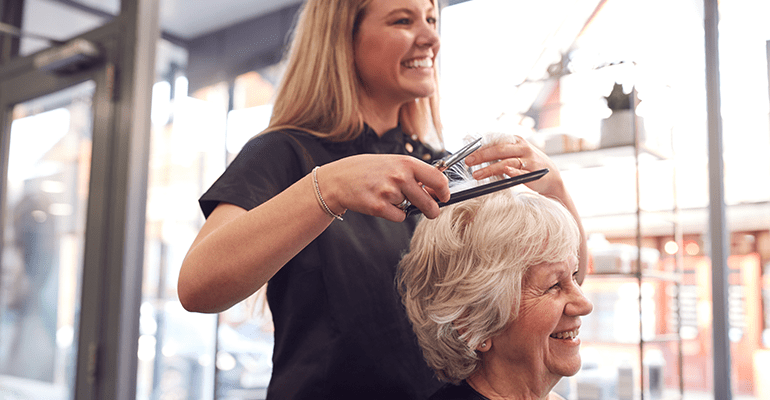 An older woman with grey hair getting her hair done by a hairdresser.