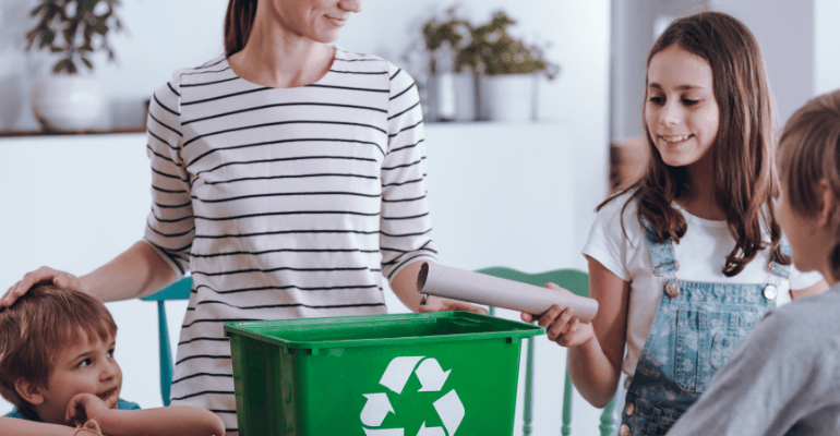 Aware mother teaching smiling children how to recycle household waste.