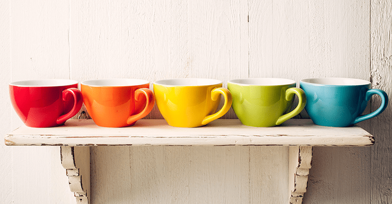 brightly coloured tea cups on a white wooden shelf on the wall - l