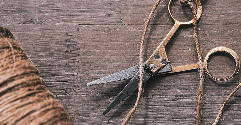 gold scissors with string tied around the handle on a wooden table - l