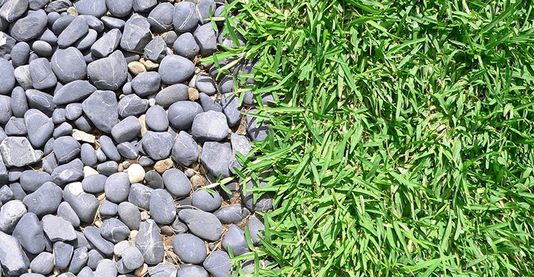 large grey pebbles next to green grass - l