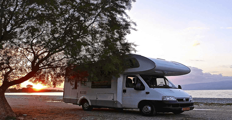 large white motorhome parked by the water under a big tree - l