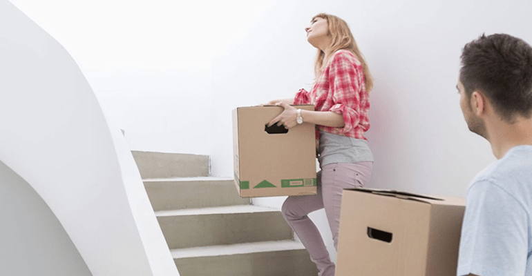 man and woman walking up a white staircase holding moving boxes - l