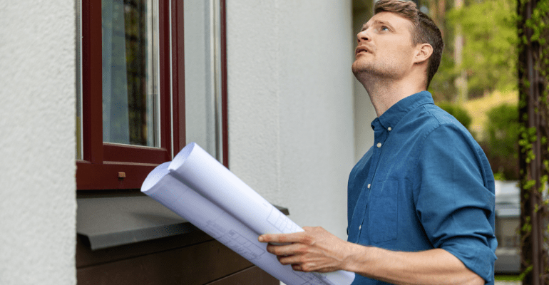 Man in blue shirt appraising the outside of a house.