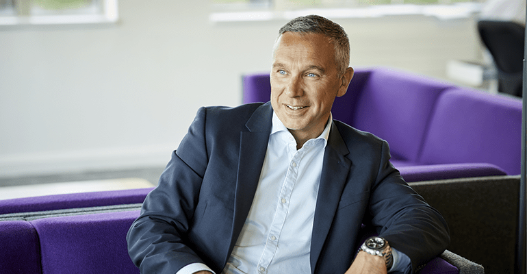 man in blue suit sat on purple sofa chris baguley - l