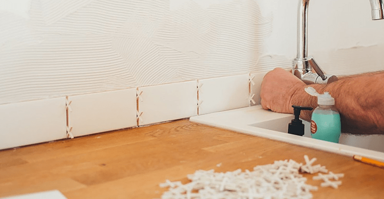 man putting up tiles next to a kitchen sink - l