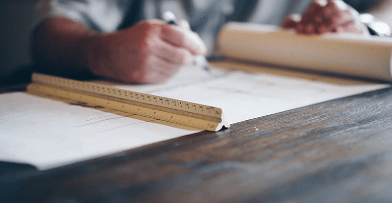 man working on a unfurled technical drawing with a ruler holding the paper down - l