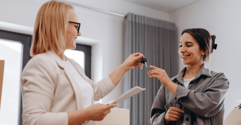 Middle aged landlady handing keys to younger female tenant.