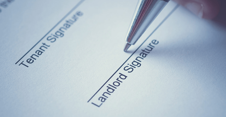 person holding a pen signing a document for tenants and landlords - l