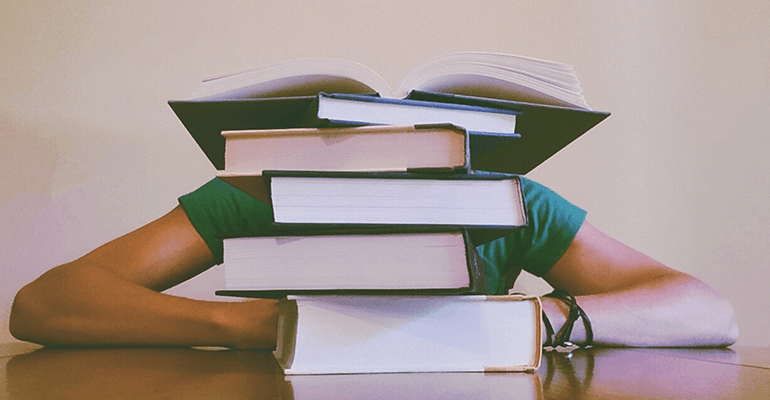 person in a green tshirt sat behind a big pile of books - l