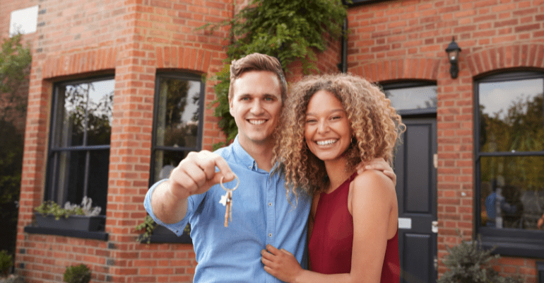 Portrait Of Excited Young Couple Standing Outside New Home Holding Keys Together