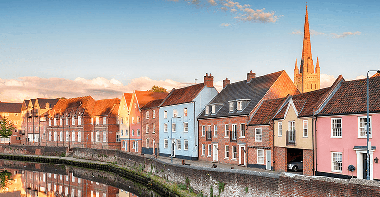 row of houses next to a river with a church behind at sunset - l