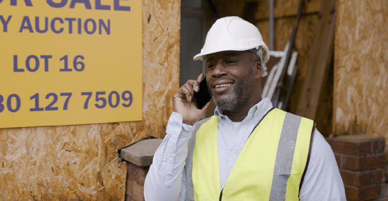 Male in a hard hat and hi vis at a building site.