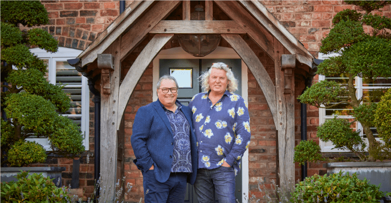 Two men smiling in front of their front door.