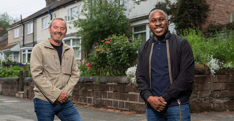 two men stood in a street smiling at the camera - l