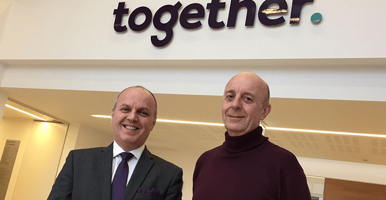 two older men stood under a Together sign - l