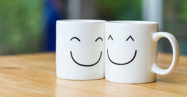 two white mugs with smiley faces on a wooden table - l