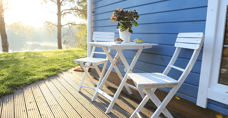 white wooden chairs and table on decking outside a blue summer house - l