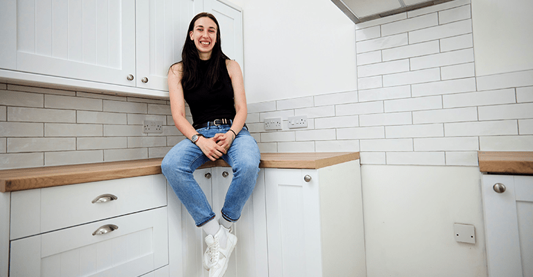 Woman sat on a kitchen counter smiling.