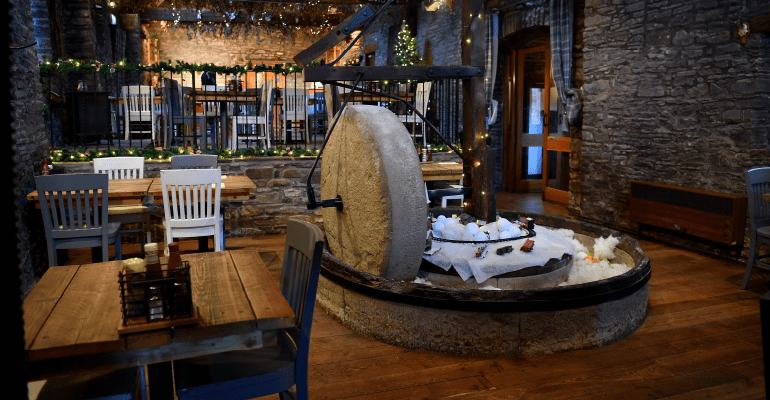 Inside of a pub with tables and chairs and a stone fire pit