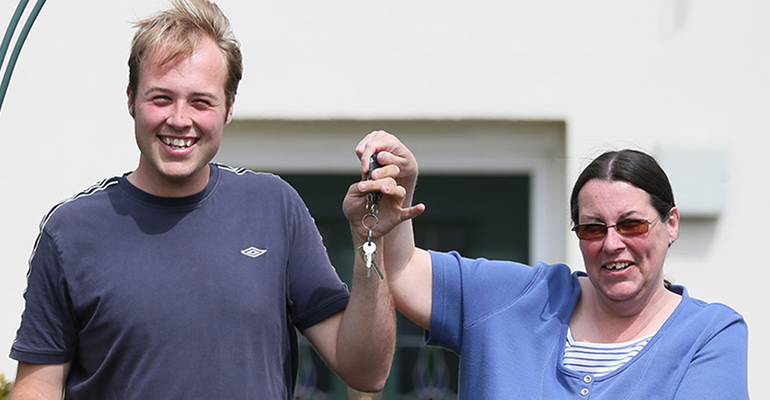 man and woman smiling holding a set of keys outside a house - l