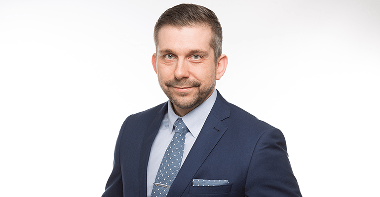 man smiling at the camera wearing a blue suit with a blue spotty tie - l