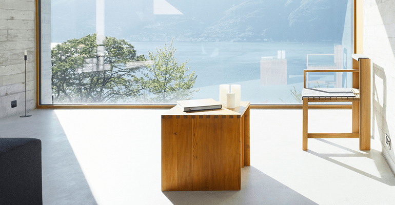 room with a modern wooden table and chair by a large window looking out over the sea - l