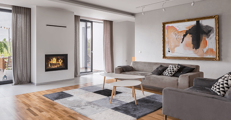 The interior of a modern house with sofas on the right, a carpet in the middle and a fireplace on the left.