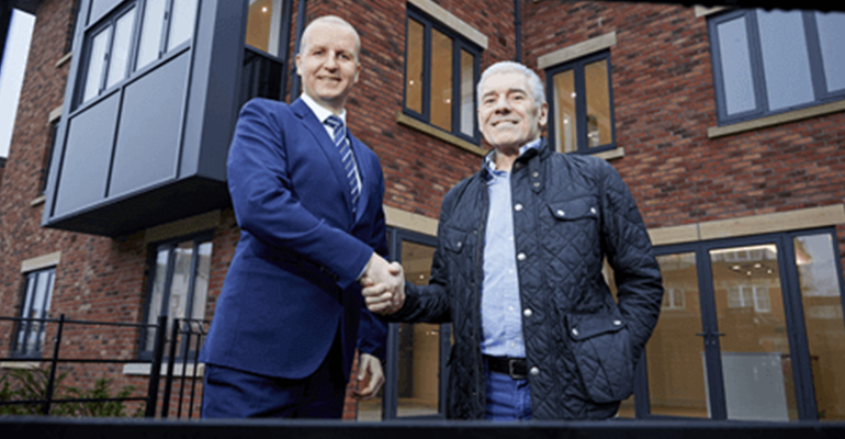 two men shaking hands outside a building - l