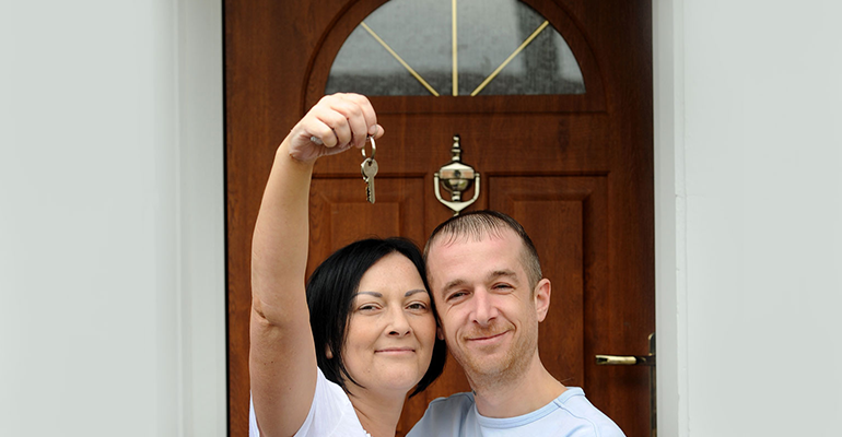 woman holding keys up hugging a man next to her smiling in front of their new front door - l