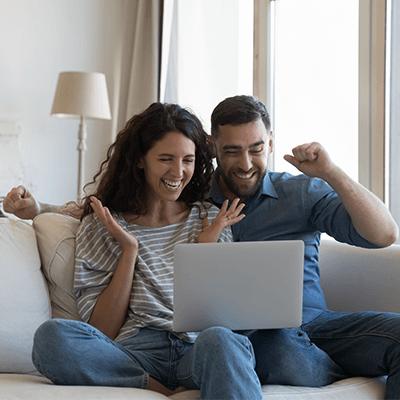 A couple looking at a laptop cheering together.