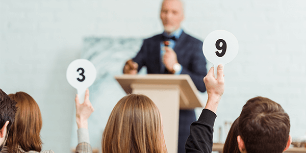 A group of people in an auction room with two people holding numbers up.