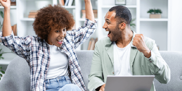 A woman and a man cheering whilst looking at a laptop.