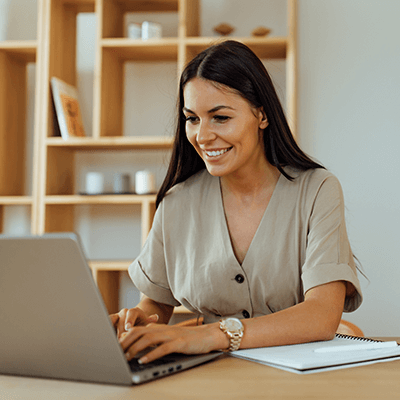 A woman smiling whilst typing on her laptop.