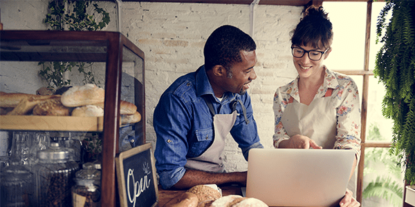 A man and a woman talking whilst pointing at a laptop in a small bakery business.